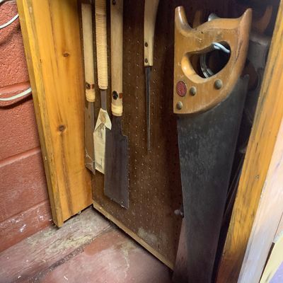 Collection of vintage hand saws, including traditional Japanese pull saws and a classic wooden-handled crosscut saw, hanging on a pegboard.