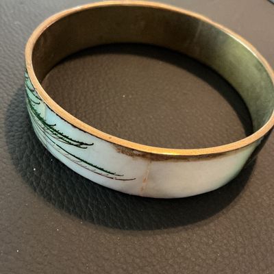 Sale Photo Thumbnail #184: Vintage enamel and brass bangle bracelet featuring a white and green feathery botanical or pine motif. Inner rim shows light patina and minor tarnish consistent with age; outer enamel shows slight wear near the seams but remains in good wearable condition