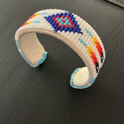Sale Photo Thumbnail #154: Hand-beaded cuff bracelet featuring colorful geometric patterns in white, blue, red, yellow, and black seed beads. The interior is lined with light-colored leather/suede. Shows minor signs of wear and light soil on the leather interior, but all beadwork a