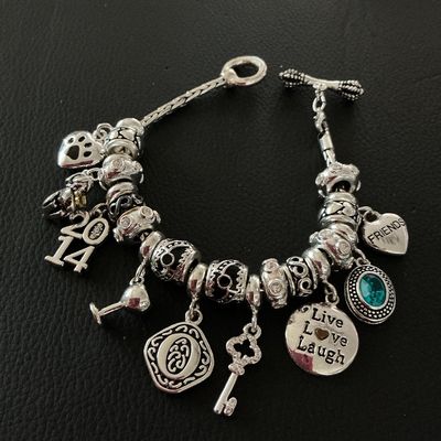 Sale Photo Thumbnail #164: Silver-tone charm bracelet with toggle closure featuring various charm pendants and decorative spacers. Charms include a paw print, "2014" date charm, wine glass, key, "Live Love Laugh" disc, "Friends" heart, and a faux turquoise stone drop. In very good 