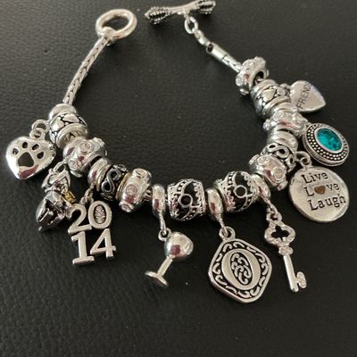 Sale Photo Thumbnail #165: Silver-tone charm bracelet with toggle closure featuring various charm pendants and decorative spacers. Charms include a paw print, "2014" date charm, wine glass, key, "Live Love Laugh" disc, "Friends" heart, and a faux turquoise stone drop. In very good 