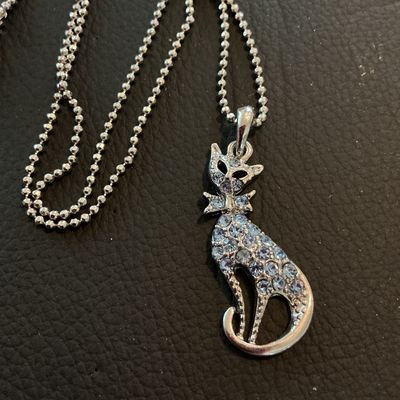 Sale Photo Thumbnail #200: Silver-tone ball chain necklace featuring a seated cat pendant encrusted with light blue rhinestones. Includes a lobster claw clasp with an extender chain. Good condition with all stones intact.