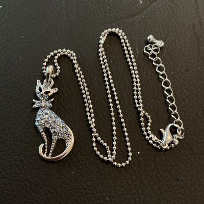 Sale Photo Thumbnail #201: Silver-tone ball chain necklace featuring a seated cat pendant encrusted with light blue rhinestones. Includes a lobster claw clasp with an extender chain. Good condition with all stones intact.