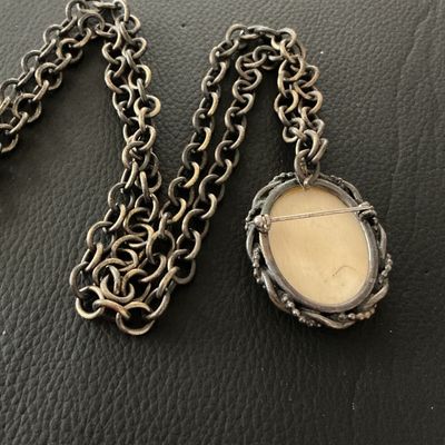 Sale Photo Thumbnail #136: A vintage oval pendant featuring a scrimshaw-style illustration of a sailing ship at sea, set within a twisted metal frame. The piece features a pin back, allowing it to be worn as a brooch, as well as a loop attached to a chunky metal link chain. The pen