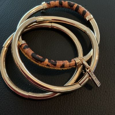 Sale Photo Thumbnail #169: Set of interlinked gold-tone metal bangle bracelets featuring leopard print fabric or hair-on-hide accents. Includes an attached metal tag stamped 'NINE WEST'. In good condition with minimal surface wear.