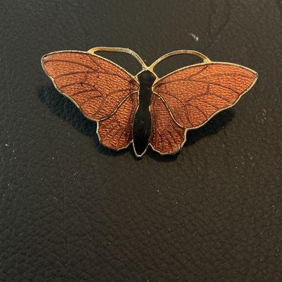 Sale Photo Thumbnail #196: Vintage butterfly-shaped brooch featuring orange translucent enamel wings with detailed vein texturing and a black center body set in gold-tone metal. Measures approximately 1.75 inches wide. Features a standard roll-over safety clasp on the reverse. Show