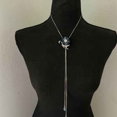 Sale Photo Thumbnail #159: Silver-tone lariat-style bolo necklace featuring a flower motif centerpiece set with marquise-cut navy/sapphire blue crystals and pavé rhinestones. Silver-tone snake chain ends with dangling blue rhinestone charm tips. Good pre-owned condition with no mi