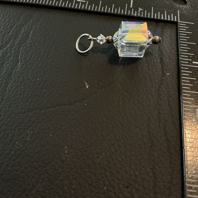 Sale Photo Thumbnail #204: Small pendant or charm featuring a cube-shaped faceted crystal with an iridescent aurora borealis coating. Accentuated with silver-tone decorative end caps, bead accents, and a top jump ring. Measures approximately 1 inch long including the ring. Good con