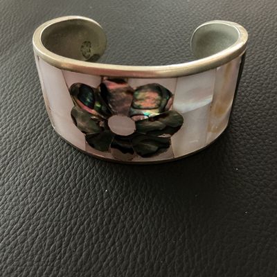 Sale Photo Thumbnail #143: Vintage Mexican cuff bracelet featuring mother of pearl inlay with a central dark abalone shell flower design. The interior is stamped 'HECHO EN MEXICO'. Shows minor surface tarnish and age-appropriate wear.