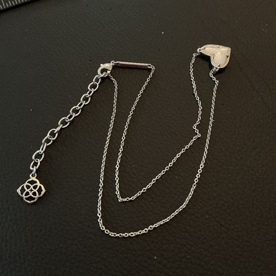 Sale Photo Thumbnail #173: A Kendra Scott silver-tone necklace featuring a heart-shaped mother of pearl (iridescent stone) pendant with a textured or pave-accented border. Includes an adjustable extender chain with the signature Kendra Scott logo charm and branded metal tag near th