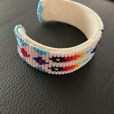 Sale Photo Thumbnail #153: Hand-beaded cuff bracelet featuring colorful geometric patterns in white, blue, red, yellow, and black seed beads. The interior is lined with light-colored leather/suede. Shows minor signs of wear and light soil on the leather interior, but all beadwork a
