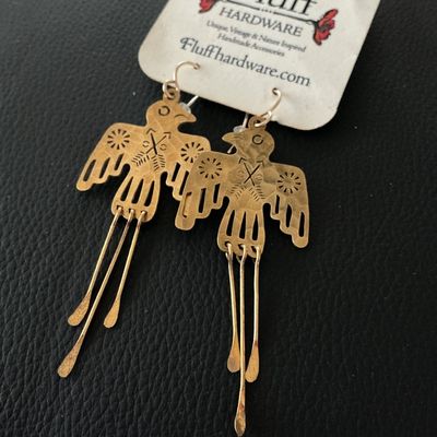 Sale Photo Thumbnail #138: Pair of Fluff Hardware 'Glide' dangle earrings featuring a brass or gold-tone Thunderbird design with hammered tail strands. Includes original carding which notes 14k gold-filled or sterling silver ear wires. Measure approximately 3 inches in overall leng