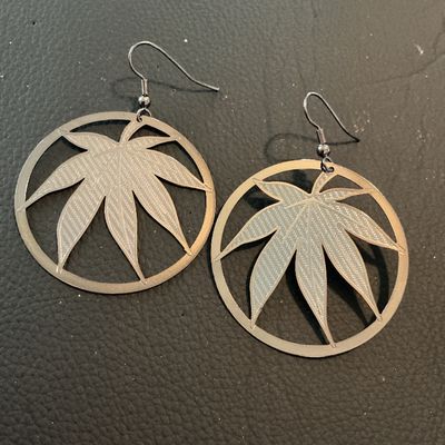 Sale Photo Thumbnail #185: Pair of circular drop dangle earrings featuring a textured cutout leaf design inside a round frame. Made of lightweight silver-tone metal with french wire ear hooks. Each circular drop measures approximately 1.75 inches in diameter. In good condition with