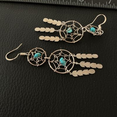 Sale Photo Thumbnail #142: Pair of silver-tone wire dreamcatcher dangle earrings featuring two webbed tiers, turquoise-colored bead accents, and hanging feather charms. Equipped with french hook ear wires. Each earring measures approximately 3 inches in length. In good pre-owned co