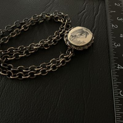 Sale Photo Thumbnail #137: A vintage oval pendant featuring a scrimshaw-style illustration of a sailing ship at sea, set within a twisted metal frame. The piece features a pin back, allowing it to be worn as a brooch, as well as a loop attached to a chunky metal link chain. The pen