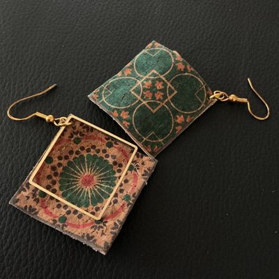 Sale Photo Thumbnail #133: A pair of lightweight dangle earrings featuring square cork bases printed with green and orange geometric tile-style floral patterns. One earring includes a square gold-tone metal frame overlay. Finished with gold-tone French wire ear hooks. Good pre-owne