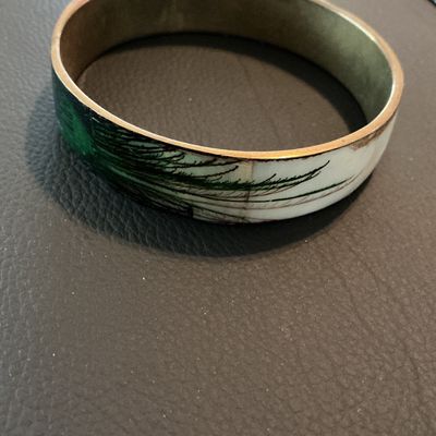 Sale Photo Thumbnail #182: Vintage enamel and brass bangle bracelet featuring a white and green feathery botanical or pine motif. Inner rim shows light patina and minor tarnish consistent with age; outer enamel shows slight wear near the seams but remains in good wearable condition