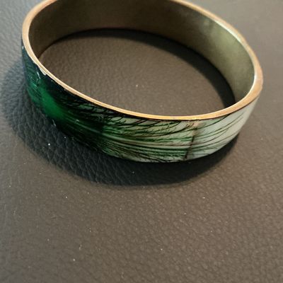 Sale Photo Thumbnail #183: Vintage enamel and brass bangle bracelet featuring a white and green feathery botanical or pine motif. Inner rim shows light patina and minor tarnish consistent with age; outer enamel shows slight wear near the seams but remains in good wearable condition