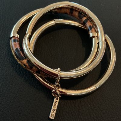 Sale Photo Thumbnail #170: Set of interlinked gold-tone metal bangle bracelets featuring leopard print fabric or hair-on-hide accents. Includes an attached metal tag stamped 'NINE WEST'. In good condition with minimal surface wear.