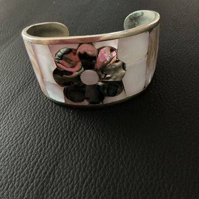 Sale Photo Thumbnail #146: Vintage Mexican cuff bracelet featuring mother of pearl inlay with a central dark abalone shell flower design. The interior is stamped 'HECHO EN MEXICO'. Shows minor surface tarnish and age-appropriate wear.