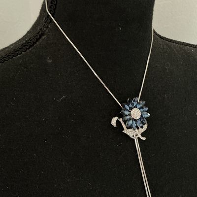 Sale Photo Thumbnail #161: Silver-tone lariat-style bolo necklace featuring a flower motif centerpiece set with marquise-cut navy/sapphire blue crystals and pavé rhinestones. Silver-tone snake chain ends with dangling blue rhinestone charm tips. Good pre-owned condition with no mi