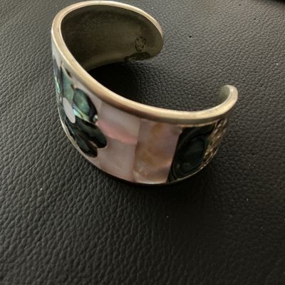 Sale Photo Thumbnail #144: Vintage Mexican cuff bracelet featuring mother of pearl inlay with a central dark abalone shell flower design. The interior is stamped 'HECHO EN MEXICO'. Shows minor surface tarnish and age-appropriate wear.