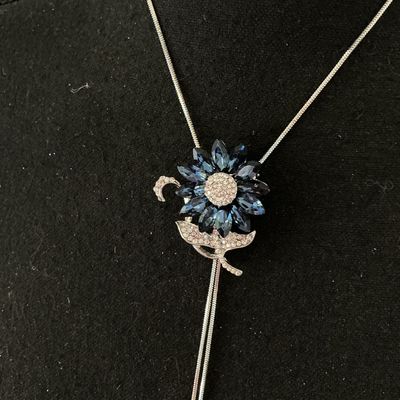 Sale Photo Thumbnail #160: Silver-tone lariat-style bolo necklace featuring a flower motif centerpiece set with marquise-cut navy/sapphire blue crystals and pavé rhinestones. Silver-tone snake chain ends with dangling blue rhinestone charm tips. Good pre-owned condition with no mi