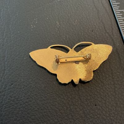 Sale Photo Thumbnail #197: Vintage butterfly-shaped brooch featuring orange translucent enamel wings with detailed vein texturing and a black center body set in gold-tone metal. Measures approximately 1.75 inches wide. Features a standard roll-over safety clasp on the reverse. Show