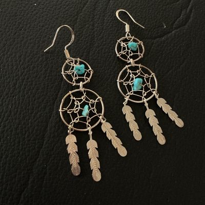 Sale Photo Thumbnail #141: Pair of silver-tone wire dreamcatcher dangle earrings featuring two webbed tiers, turquoise-colored bead accents, and hanging feather charms. Equipped with french hook ear wires. Each earring measures approximately 3 inches in length. In good pre-owned co