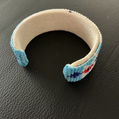 Sale Photo Thumbnail #155: Hand-beaded cuff bracelet featuring colorful geometric patterns in white, blue, red, yellow, and black seed beads. The interior is lined with light-colored leather/suede. Shows minor signs of wear and light soil on the leather interior, but all beadwork a