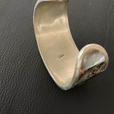 Sale Photo Thumbnail #145: Vintage Mexican cuff bracelet featuring mother of pearl inlay with a central dark abalone shell flower design. The interior is stamped 'HECHO EN MEXICO'. Shows minor surface tarnish and age-appropriate wear.