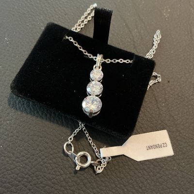 Sale Photo Thumbnail #194: Silver-tone chain necklace featuring a drop pendant set with three graduated round-cut clear cubic zirconia stones. Includes attached retail tag marked 'CZ PENDANT'. Fastens with a spring ring clasp. Comes displayed on a black velvet pad. Excellent condit