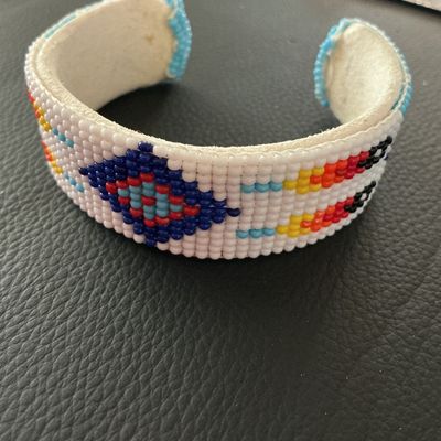 Sale Photo Thumbnail #152: Hand-beaded cuff bracelet featuring colorful geometric patterns in white, blue, red, yellow, and black seed beads. The interior is lined with light-colored leather/suede. Shows minor signs of wear and light soil on the leather interior, but all beadwork a