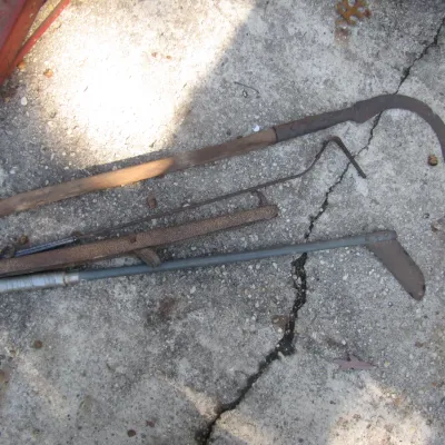Sale Photo Thumbnail #141: Collection of vintage hand tools including a long-handled scythe and manual yard equipment, showing heavy rust and age-related wear.