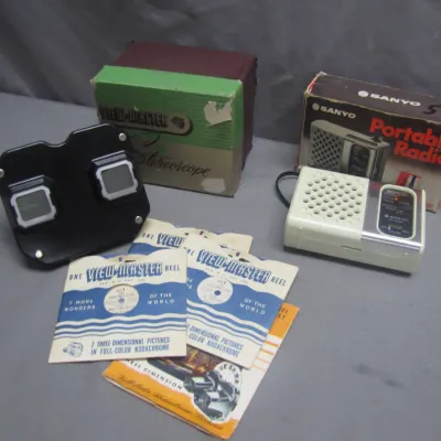 Sale Photo Thumbnail #258: Vintage Sawyer's View-Master stereoscope viewer with original box and reels, shown alongside a Sanyo portable transistor radio with its original packaging.