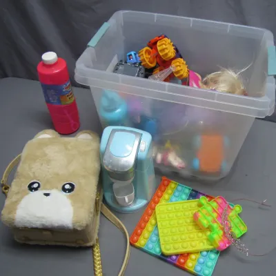Sale Photo Thumbnail #276: Assortment of children's toys and accessories including a clear storage tub filled with toys, plush bear bag, toy coffee maker, pop-it fidget toys, and bubble solution.