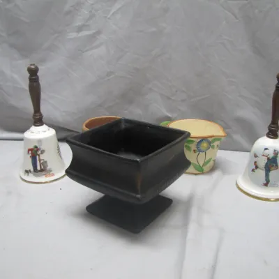 Sale Photo Thumbnail #230: Collection of decorative items including a pair of holiday-themed porcelain hand bells with wooden handles, a dark matte pedestal planter, and a floral ceramic pitcher.
