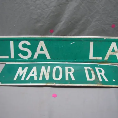 Sale Photo Thumbnail #154: Pair of vintage green and white reflective metal street signs reading 'LISA LA' and 'MANOR DR.' with minor surface wear and weathering.