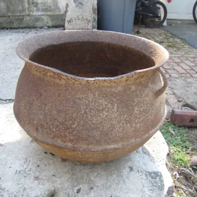 Sale Photo Thumbnail #134: Large vintage cast iron cauldron or pot with heavy surface rust and a flared rim, sitting outdoors on a concrete slab.