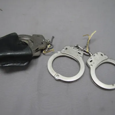 Sale Photo Thumbnail #185: Two pairs of vintage steel handcuffs with keys, including one pair housed in a black leather belt pouch.