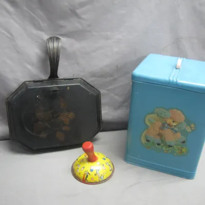 Sale Photo Thumbnail #87: Vintage tin collectibles, including a black silent butler with floral detail, a blue kitchen canister featuring a poodle design, and a small colorful spinning toy.