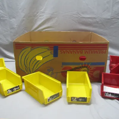 Sale Photo Thumbnail #226: Assortment of stackable plastic parts bins in yellow and red, accompanied by a cardboard banana box.