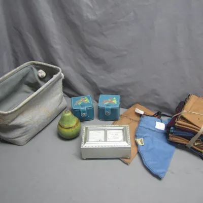 Sale Photo Thumbnail #286: Assortment of small home accessories and linens, including a fabric storage bin with rope handles, small leatherette jewelry cases, a ceramic pear container, a silver-tone photo music box, and a stack of cloth napkins.