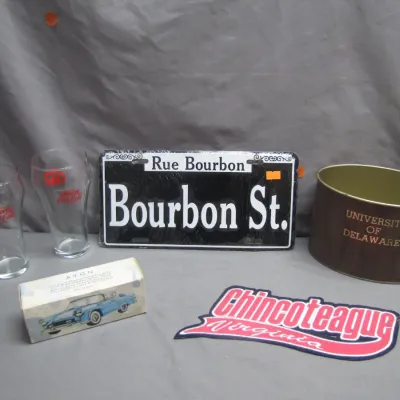 Sale Photo Thumbnail #26: Collection of souvenir and vintage items including a Bourbon St. novelty sign, two Cherry Coca-Cola drinking glasses, an Avon Ford Thunderbird decanter box, a University of Delaware metal tin, and a Chincoteague Virginia decal.