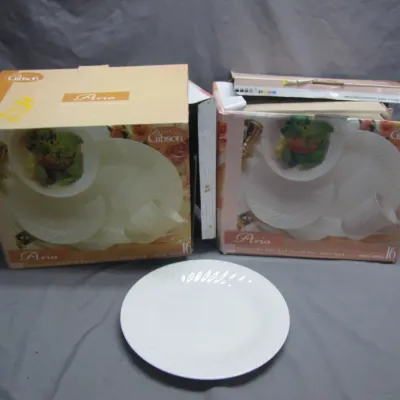 Sale Photo Thumbnail #129: Two boxed Gibson Everyday 'Aria' 16-piece dinnerware sets alongside an unboxed white ceramic plate.