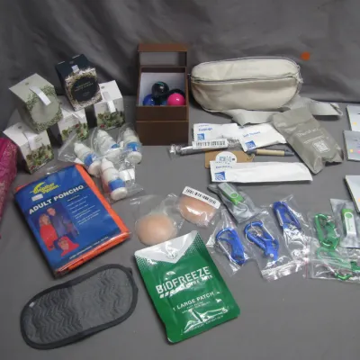 Sale Photo Thumbnail #31: Assortment of travel, wellness, and novelty items including an adult rain poncho, Biofreeze patches, carabiners, small pouches, and boxed candles.