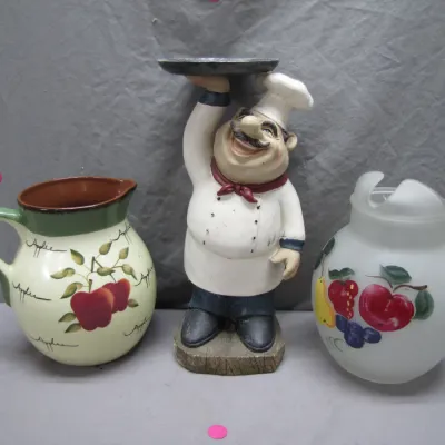 Sale Photo Thumbnail #148: Novelty kitchen decor trio including an apple-patterned ceramic pitcher, a chef figurine tray holder, and a fruit-motif frosted glass container with a broken lid.