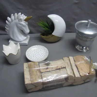 Sale Photo Thumbnail #175: Collection of home decor items including a white ceramic unicorn bust with a gold horn, a moon-shaped planter, a lidded pewter vessel, and a wrapped bundle of birch wood pieces.