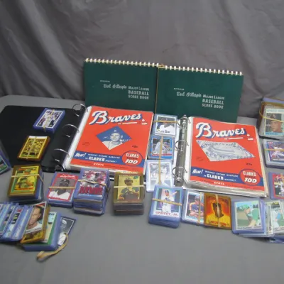 Sale Photo Thumbnail #270: Collection of vintage baseball memorabilia including Earl Gillespie scorebooks, Braves program albums, and stacks of trading cards in protective sleeves.