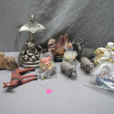 Sale Photo Thumbnail #147: Collection of assorted vintage figurines, featuring a pewter-tone teddy bear carousel music box, animal figures including camels, elephants, and a bull, and clown collectibles.